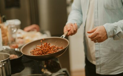 Iemand bakt gesneden groente in een koekenpan op een gasfornuis