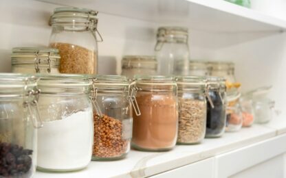 Een rij glazen weckpotten met meel, linzen en cacao op een wit schap